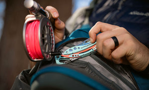 Translation missing: en.Person holding a Paradise Leatherman Skeletool® CX multi-tool next to a fishing pole and backpack