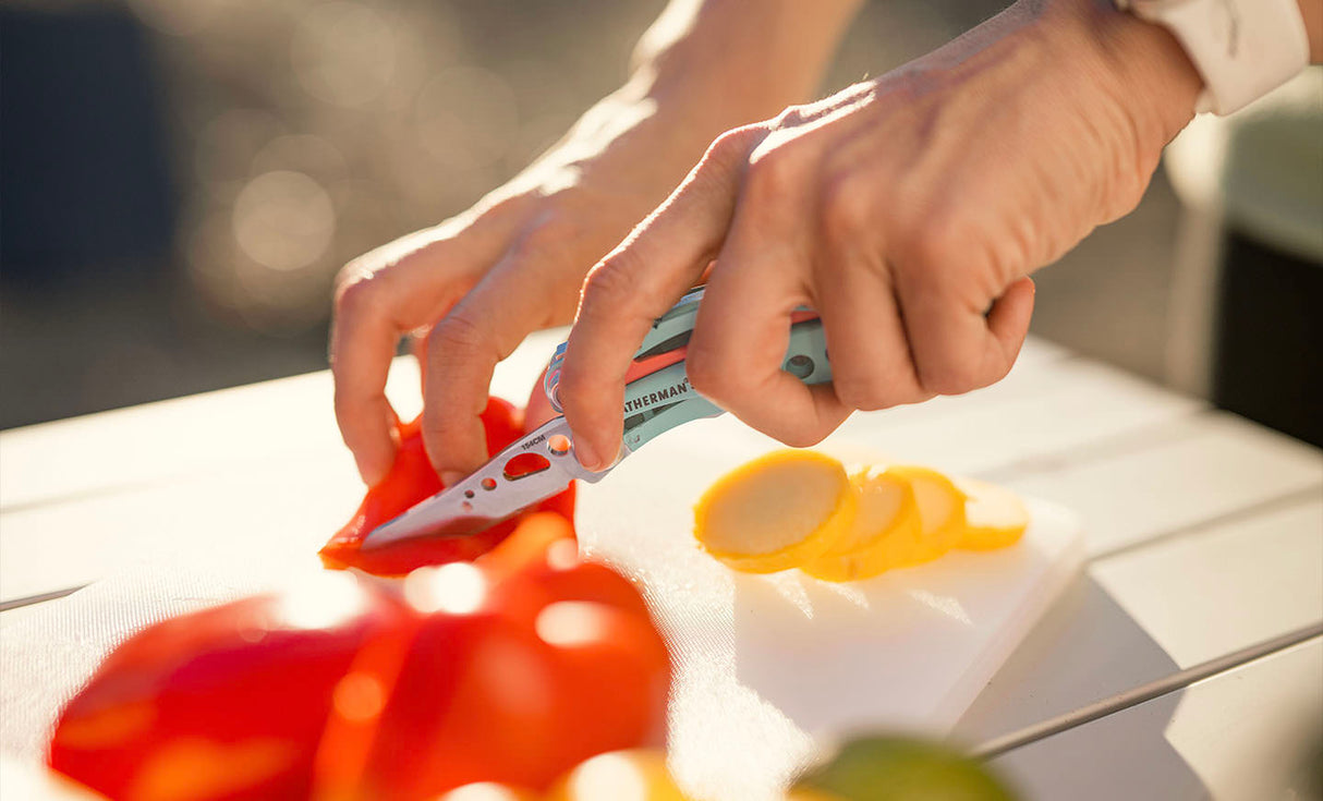 Translation missing: en.Person using a Paradise Leatherman Skeletool® CX to slice colorful vegetables on a cutting board outdoors