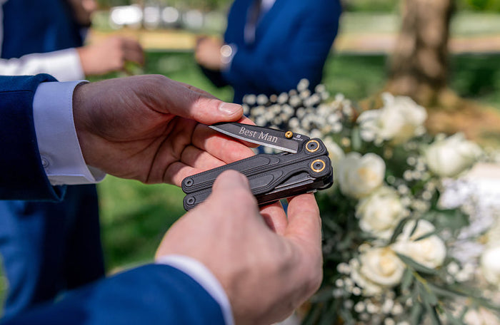 Translation missing: en.Man holding a Wave® Alpha with 'Best Man' engraving at an outdoor wedding, surrounded by guests