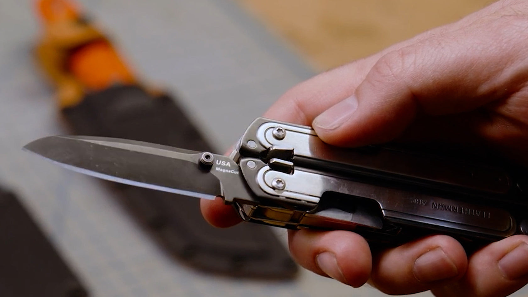 Translation missing: en.Hand holding an ARC multi-tool with a Magnacut blade extended on a blurred background